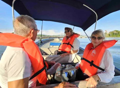 Three travelers in orange life jackets under a boat canopy on the water of the panama monkey island tour