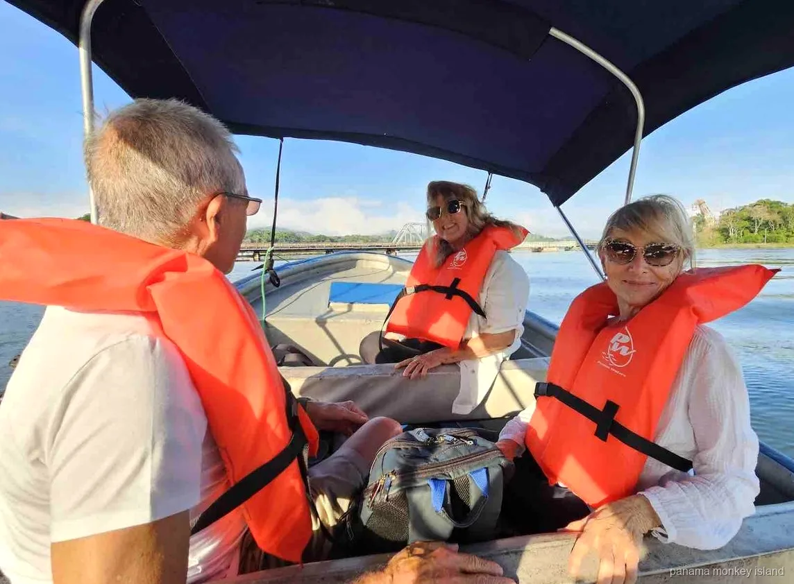 Three travelers in orange life jackets under a boat canopy on the water of the panama monkey island tour