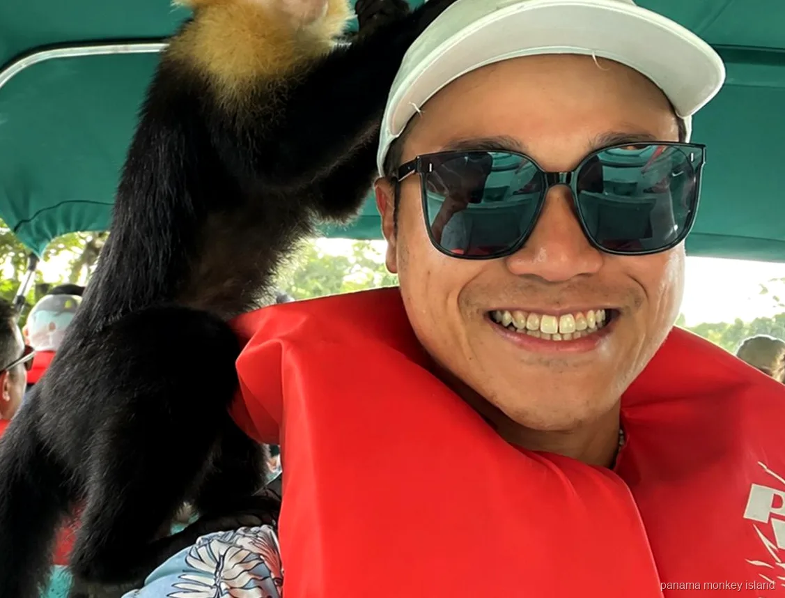 Smiling visitor in a life jacket with a capuchin monkey on the shoulder under a boat canopy on panama monkey island
