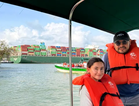 Two travelers in life jackets watch a large container ship cross the Panama Canal on a panama monkey island boat tour